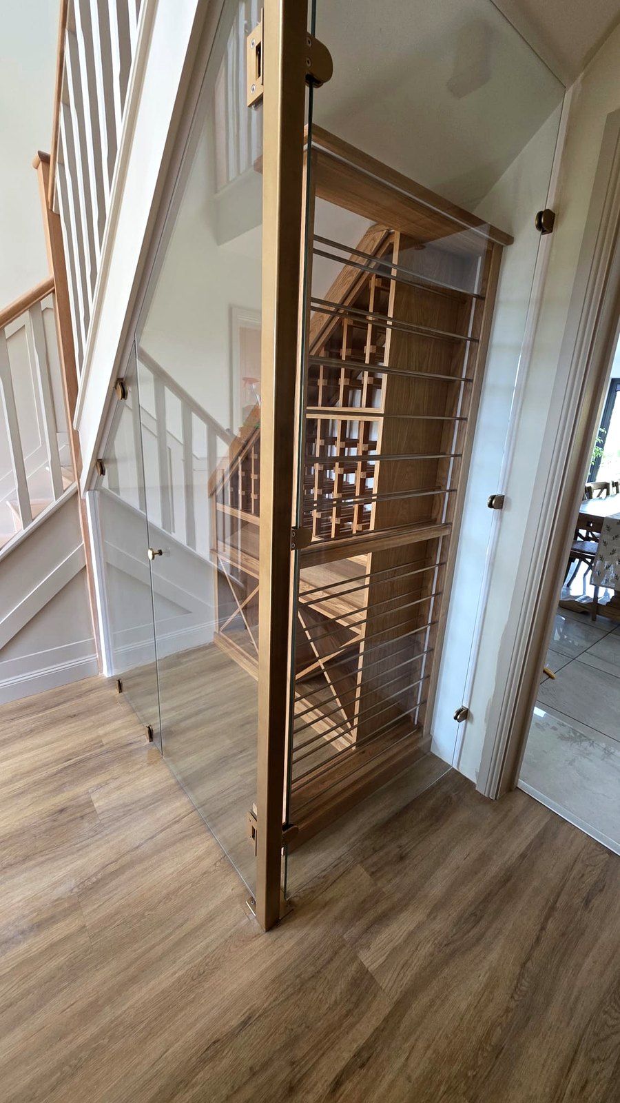 Brass pull handle and brass-matched painted corner post on a glass under-stairs wine store door, Cheshire